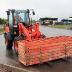 A man in a orange truck carrying crates outside an industrial building